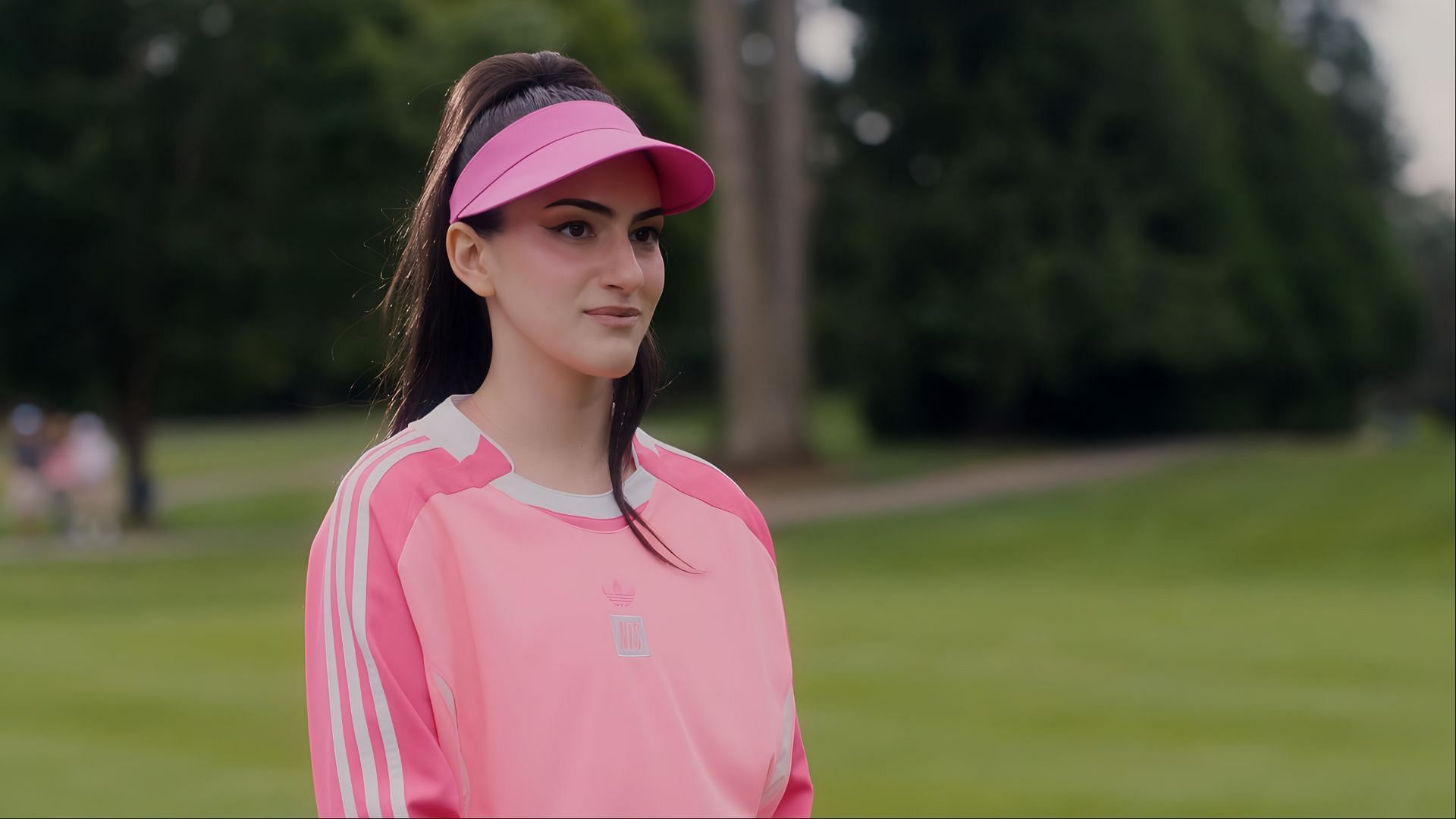 Lilli Kay as Zero in Stick wearing a pink tracksuit and visor, standing on a golf course.