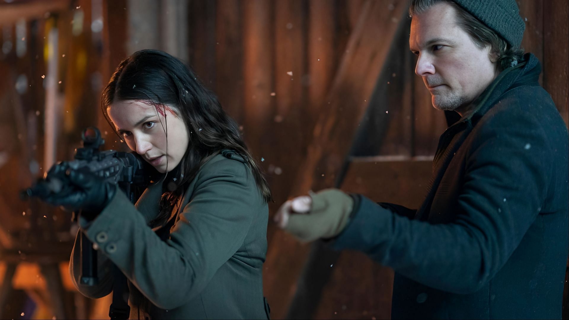 Ana de Armas aiming a rifle in a snowy setting while standing beside Norman Reedus, both dressed for winter in a tense moment from Ballerina (2025).