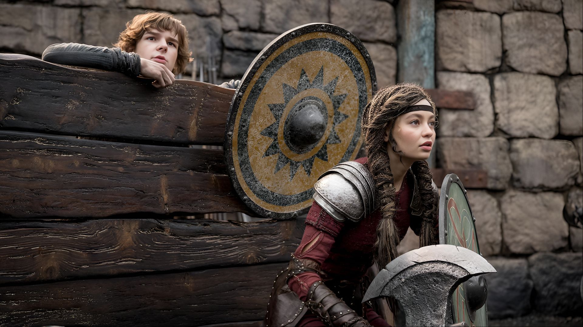 Astrid and Hiccup brace themselves behind shields in a tense moment from How To Train Your Dragon (2025). (Image via Universal)