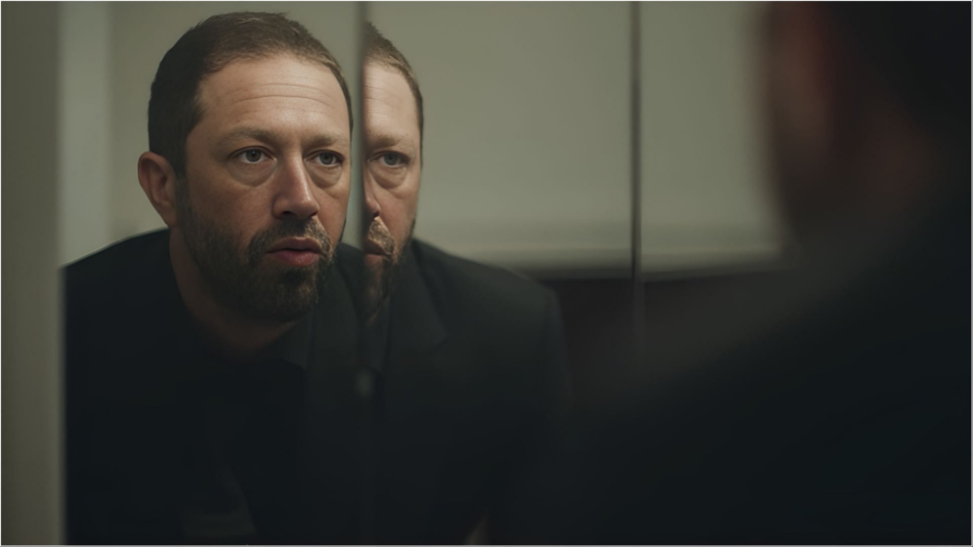 Ebon Moss-Bachrach as Richie looking at his reflection in a mirror, appearing contemplative.