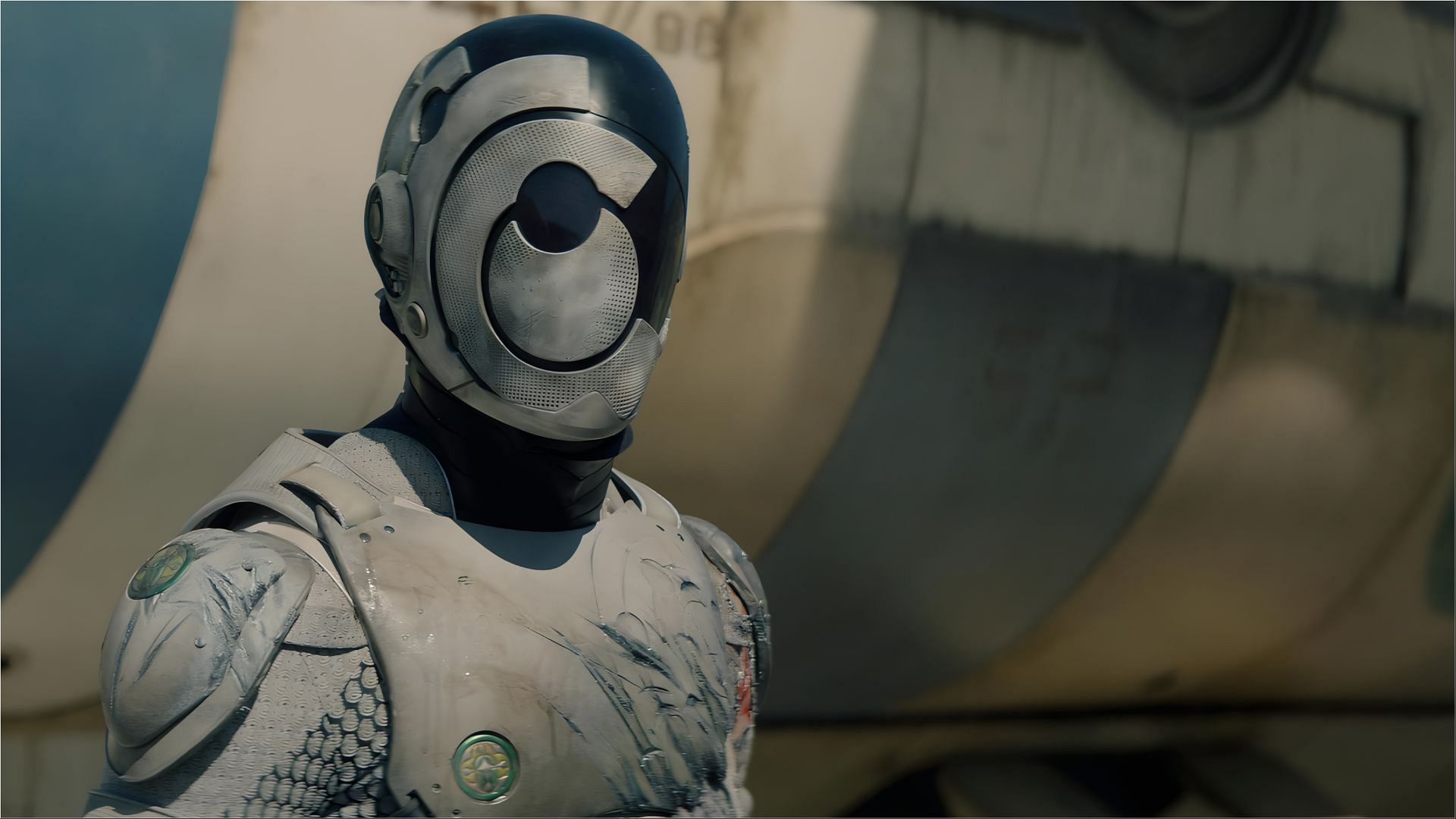 A close-up of the armored Murderbot with visible damage on its suit, standing in front of a spacecraft.
