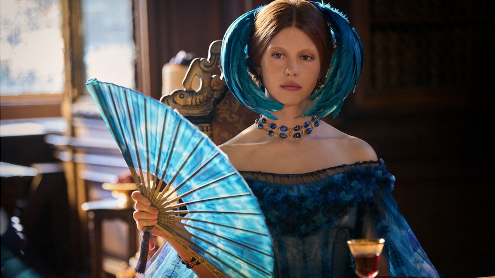 Mia Goth as Elizabeth in Frankenstein 2025, adorned in peacock feathers and saturated blue tones to reflect the film&rsquo;s operatic design language. (Image via Netflix)