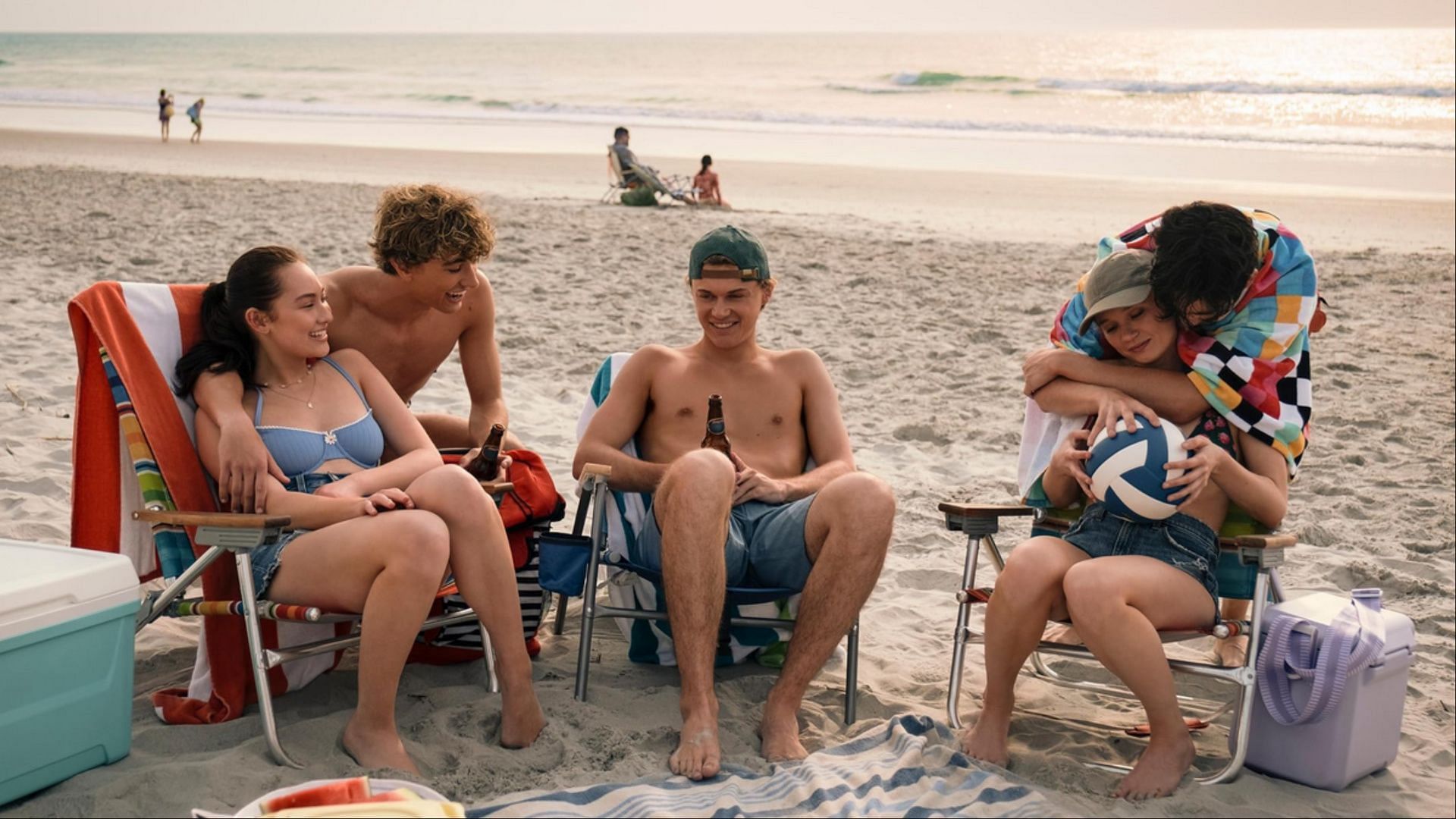 The Summer I Turned Pretty season 3 cast including Belly, Jeremiah, Steven, Taylor, and Conrad sitting together on the beach.