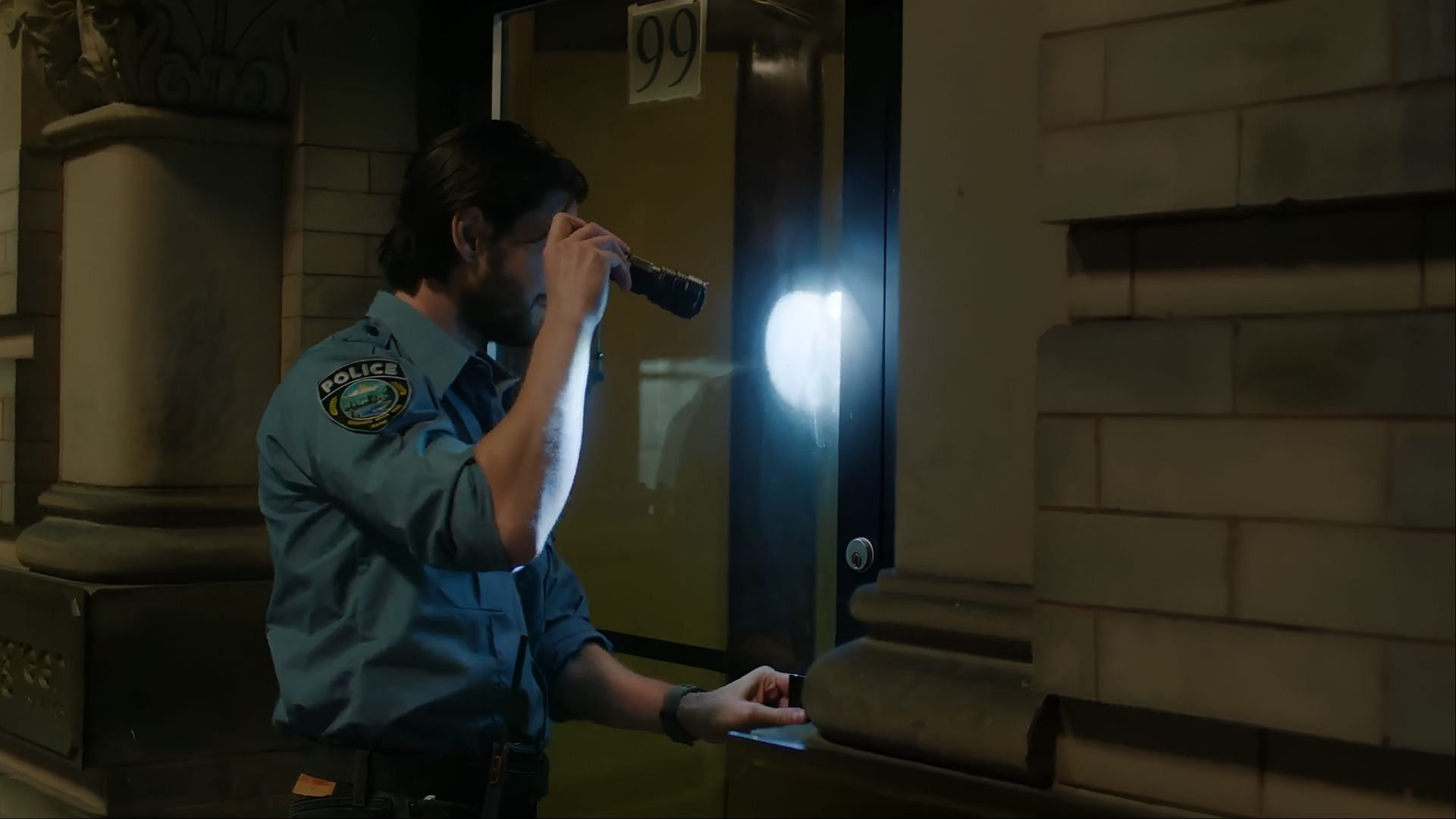 Ben Barnes as Tim Jamieson shining a flashlight on a building door during a night patrol in The Institute season 1.