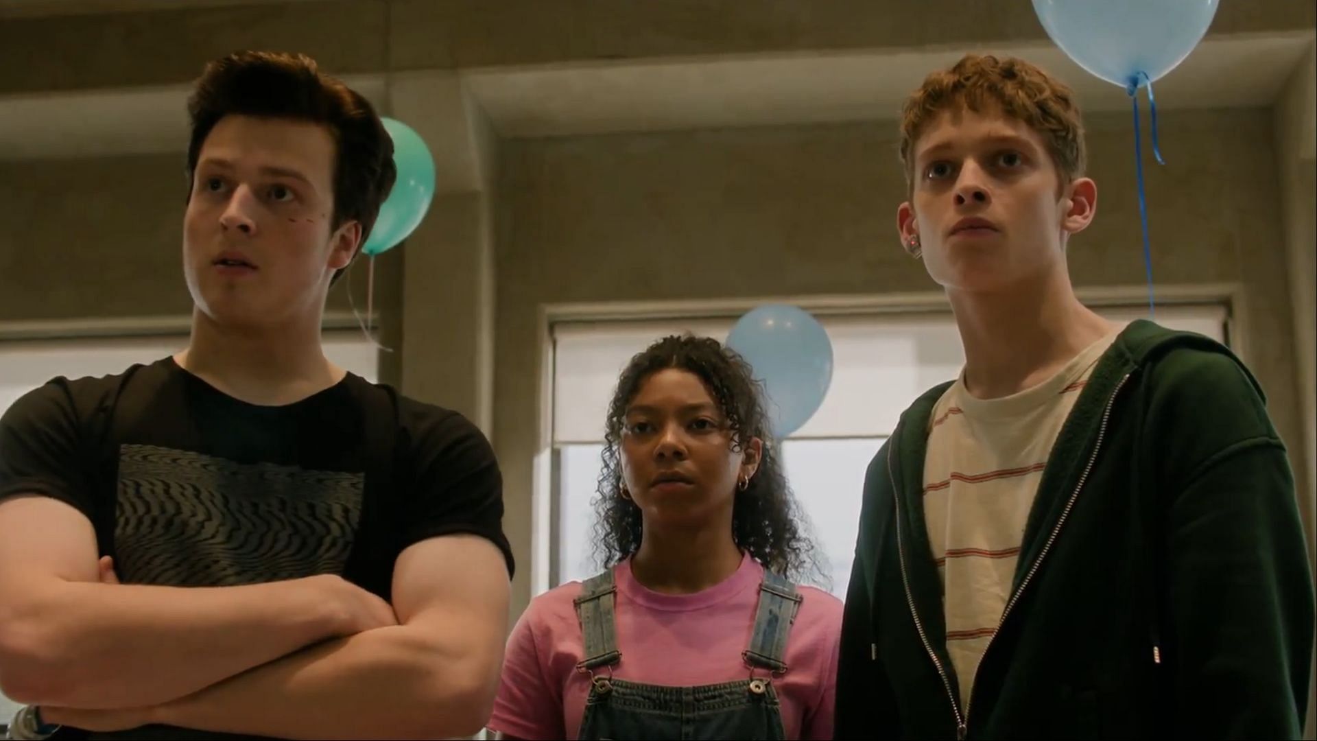 Nick, Kalisha, and Luke stand tensely under blue balloons in The Institute season 1.