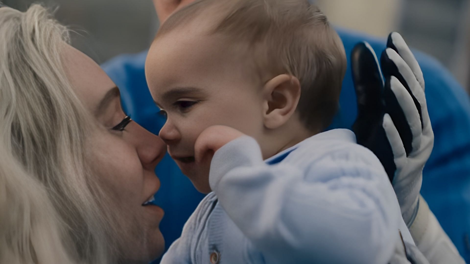 Close-up of baby Franklin Richards gently touching his mother&rsquo;s nose while his father watches in the background, dressed in blue suit.