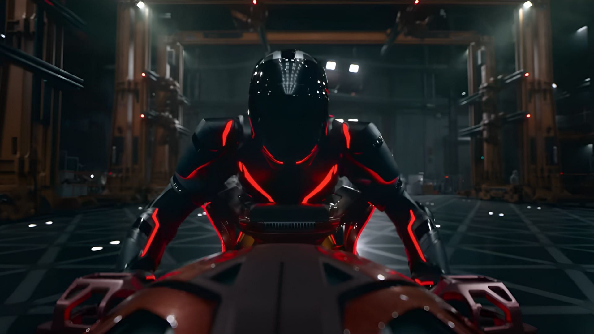 Ares, dressed in a black suit with red neon lines, sits on a futuristic bike inside a high-tech industrial facility in Tron: Ares (2025).