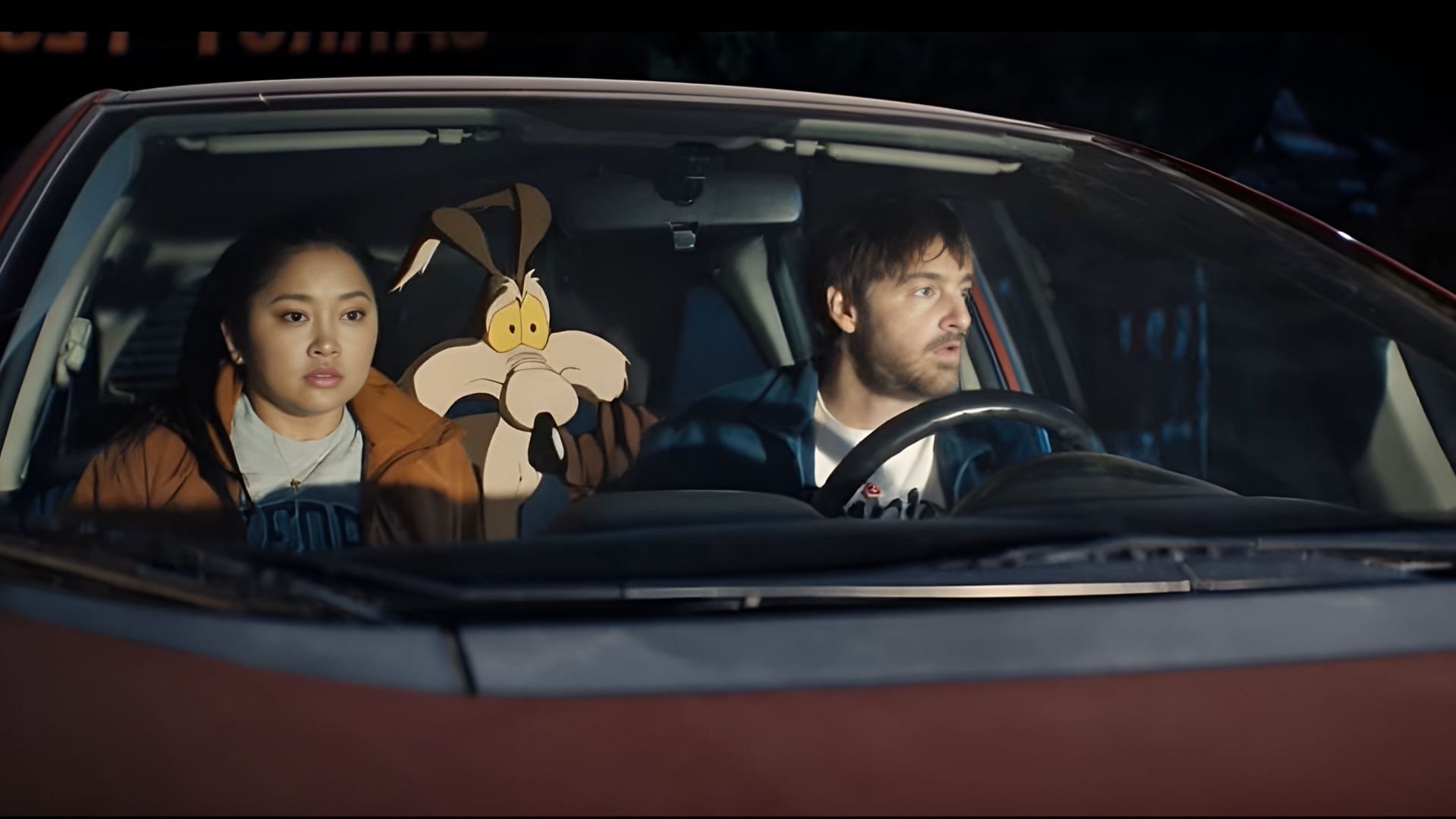 Lana Condor, Wile E. Coyote, and Will Forte take an anxious night drive in Coyote vs. Acme. The film blends live-action and animation for a new Looney Tunes courtroom adventure. (Image via  Warner Bros. Pictures/Ketchup Entertainment)