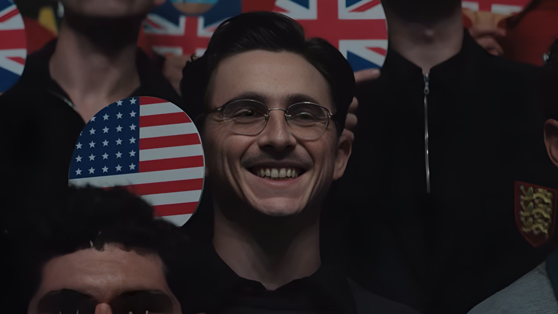 A cheering crowd scene in Marty Supreme shows spectators waving American flags at a major table tennis event. (Image via A24)