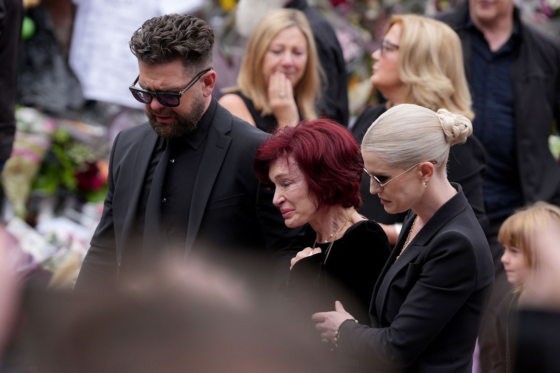 Jack Osbourne, Sharon Osbourne, and Kelly Osbourne arrive to view tributes to the late Ozzy Osbourne from fans as his funeral cortege travels through his home city of Birmingham on July 30, 2025 (Image via Getty)