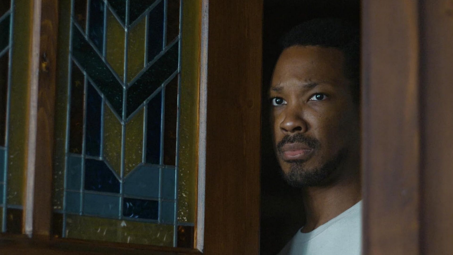 Corey Hawkins as Charles Blakey looking out through a doorway with stained glass in The Man In My Basement.