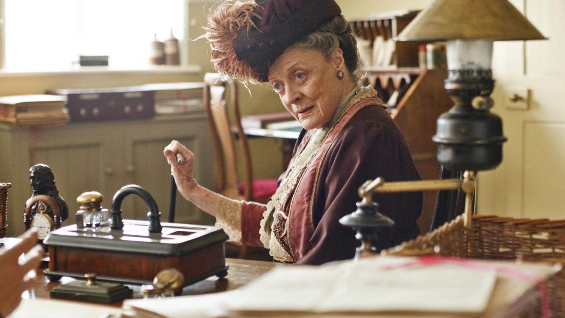 Maggie Smith portrays Violet Crawley sitting at a desk in Downton Abbey: The Grand Finale.