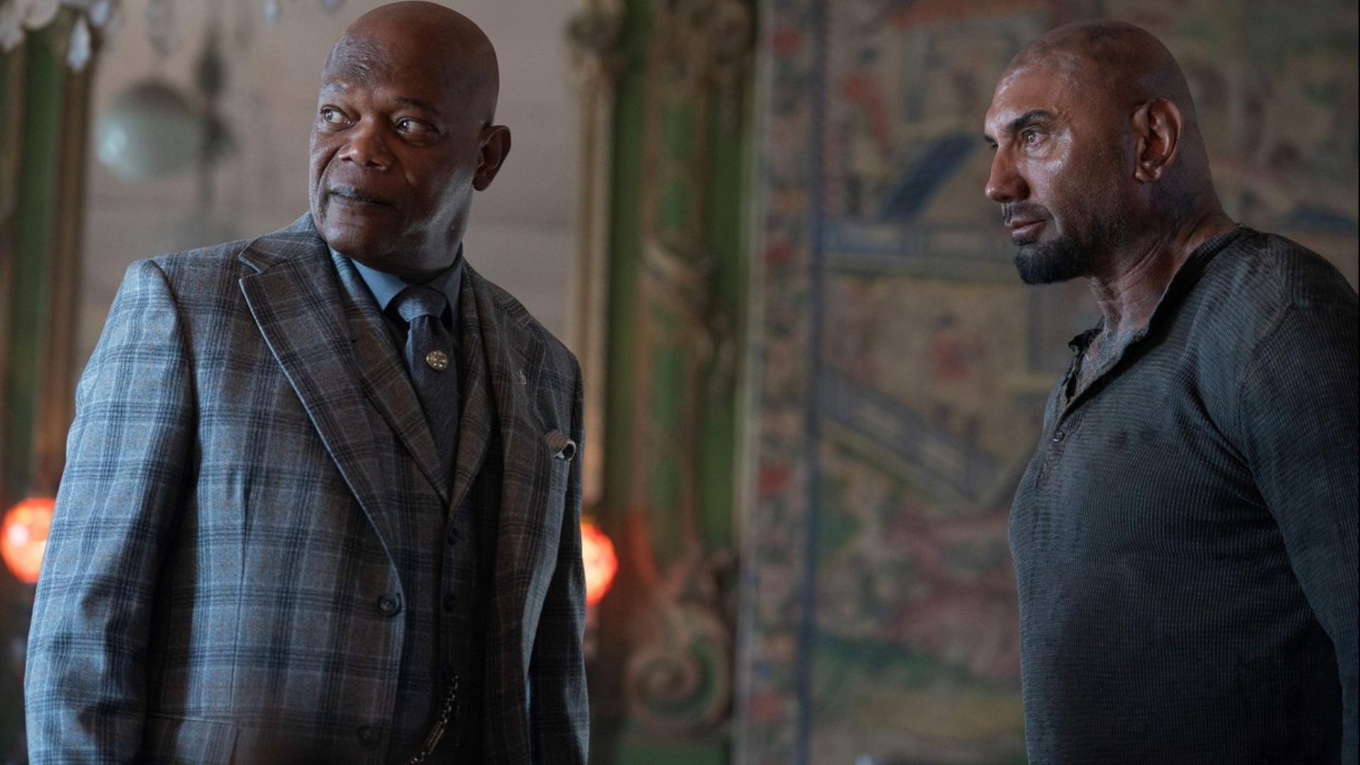 Samuel L. Jackson in a suit stands beside Dave Bautista in a dark shirt during a tense exchange.