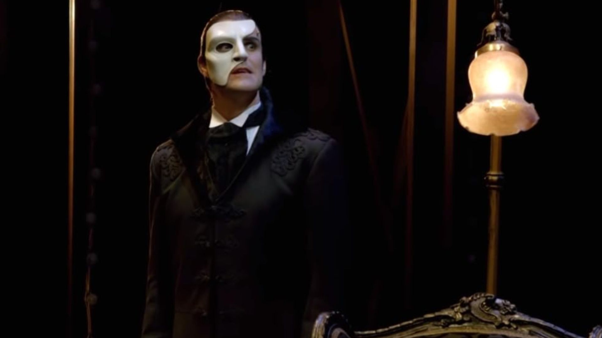  Ben Lewis performing as The Phantom in Love Never Dies, wearing a half mask and dark suit on stage.