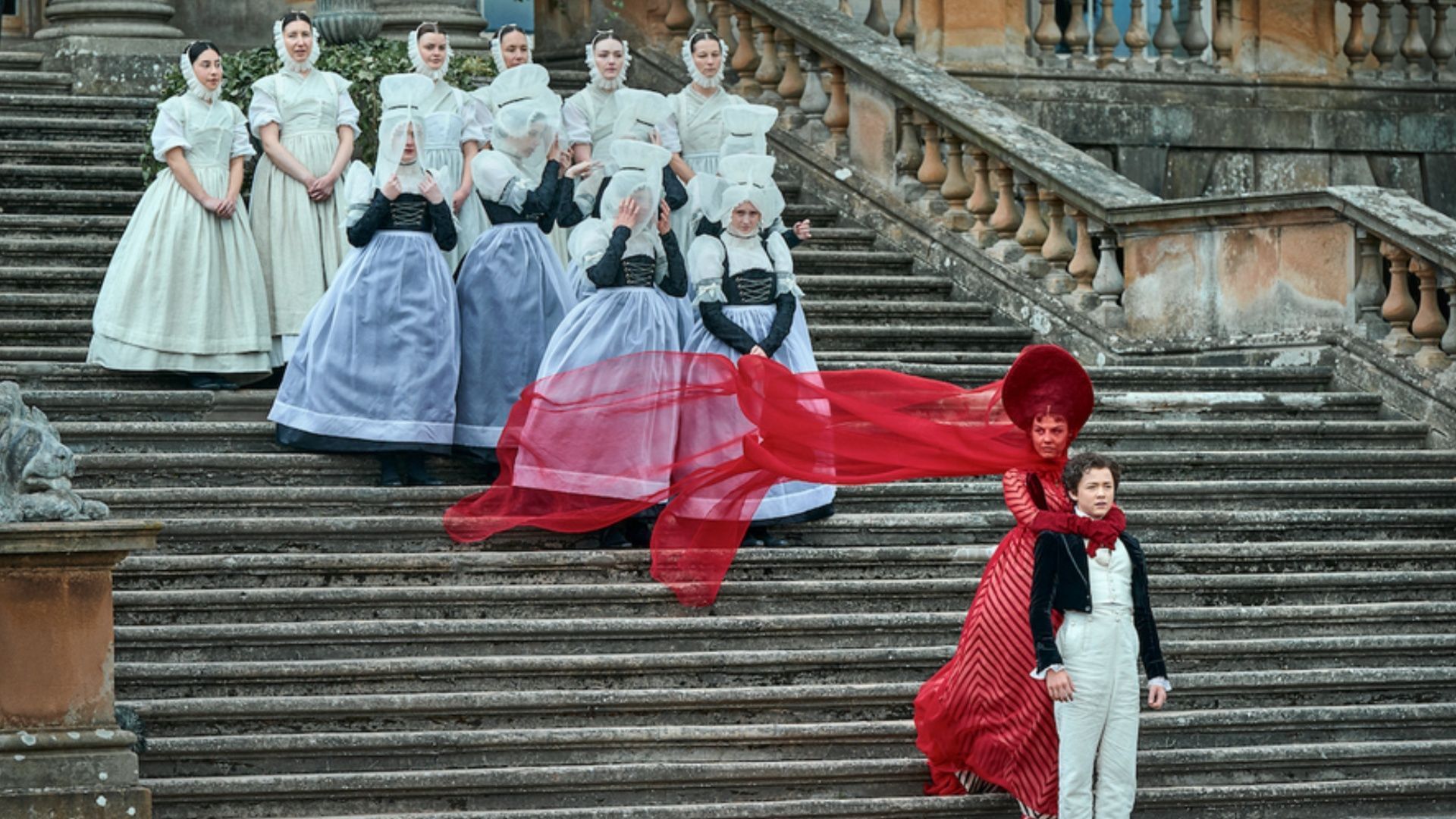 A striking visual from the Frankenstein trailer highlights period costumes and gothic atmosphere, featuring a dramatic red-clad character on the grand staircase. (Image via Netflix)