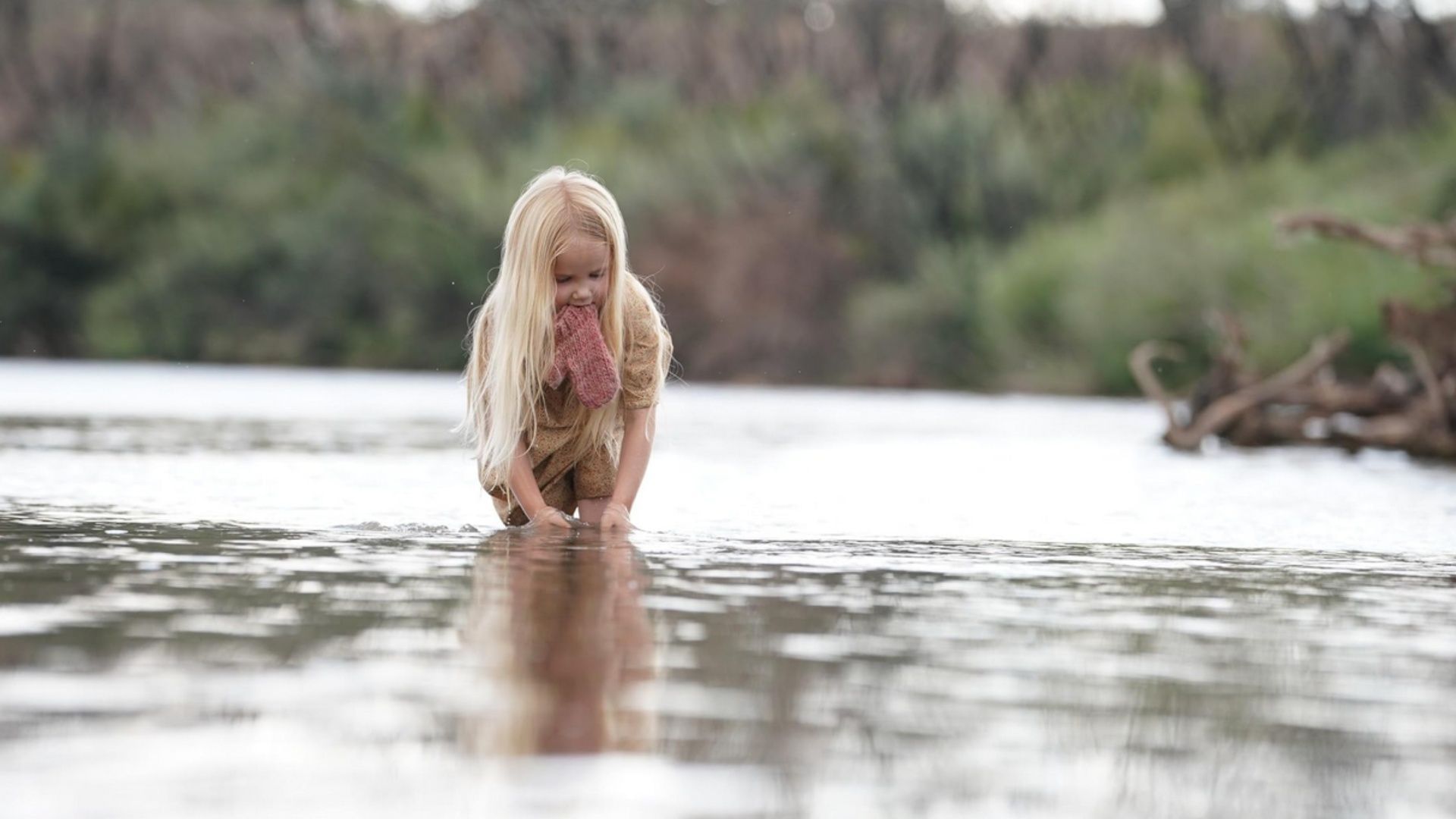 The girl crouches in the river, a haunting image that reflects purity, danger, and rebirth in Killing Faith. (Image via Shout! Studios)