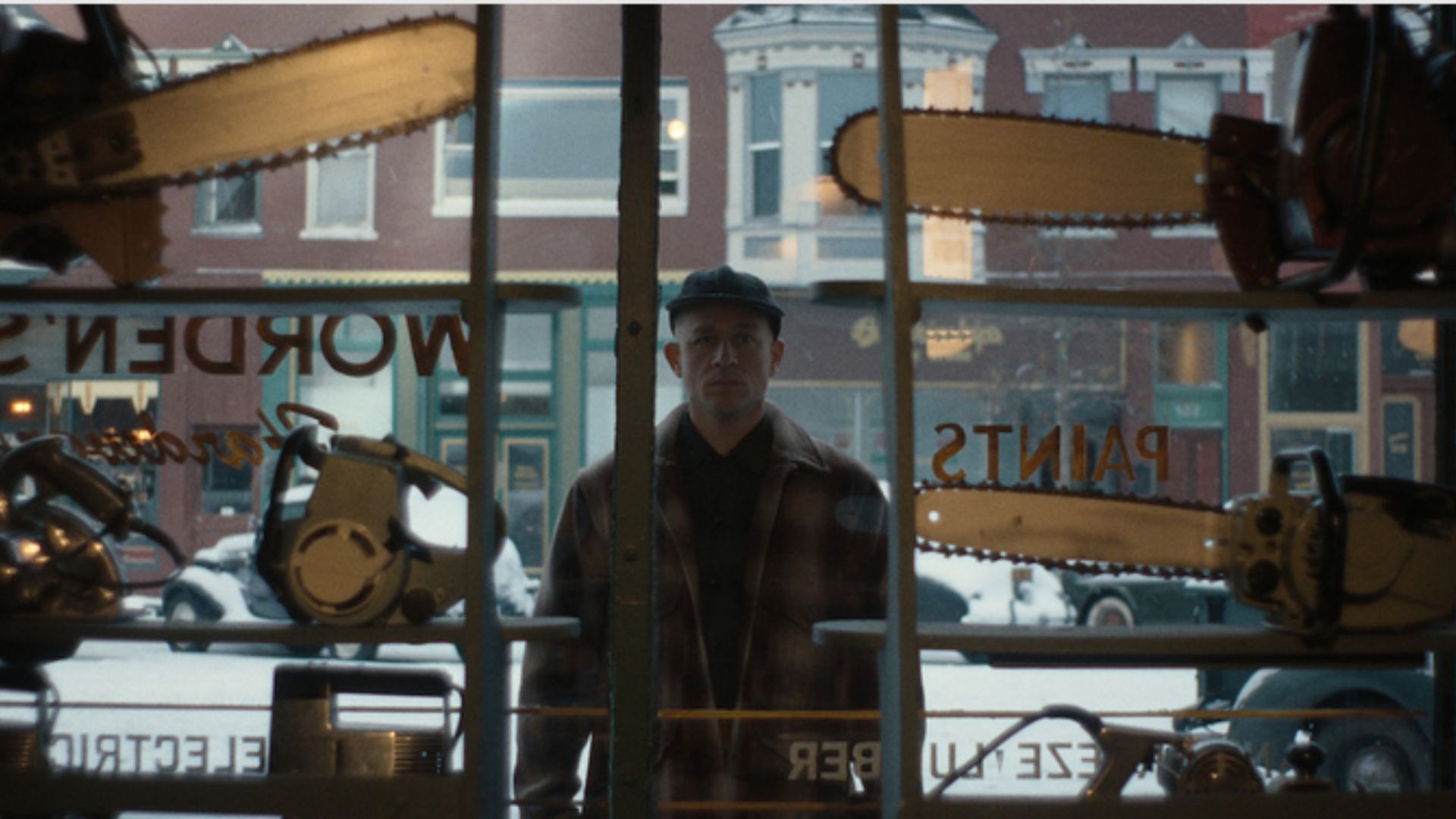 Charlie Hunnam stands outside a store, staring through the window at chainsaws on display, in a scene from Monster: The Ed Gein Story