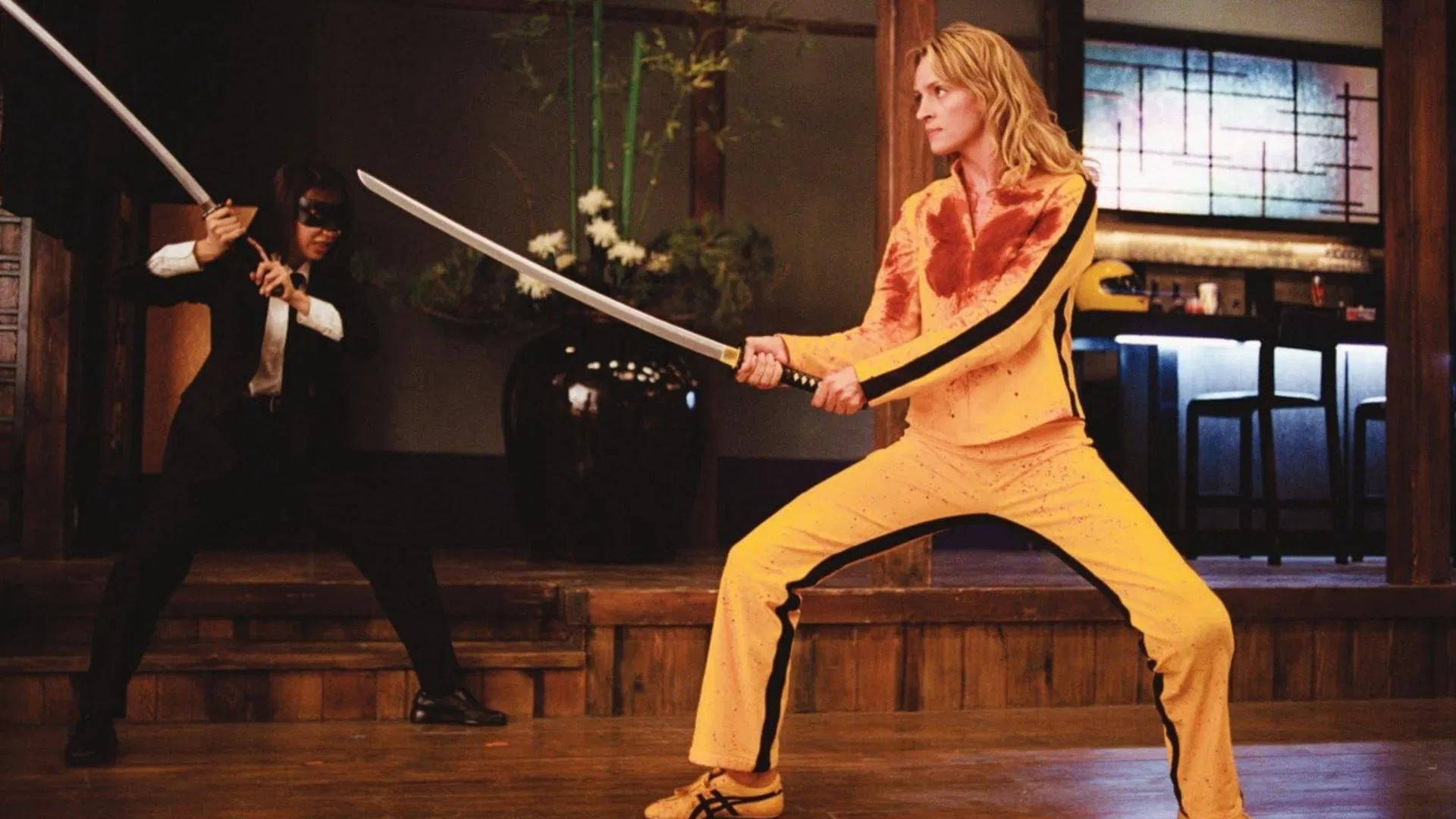 Two figures facing each other with katanas drawn inside a wooden interior; one wears a yellow tracksuit.