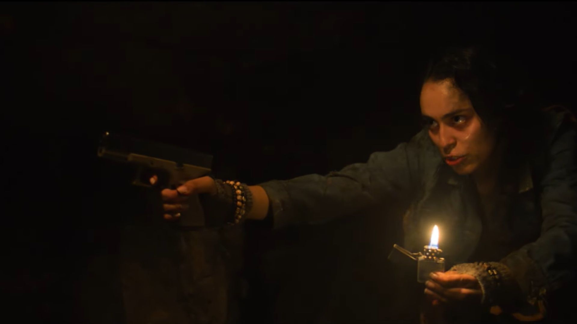 Emalia as Kate in Scurry (2025) cautiously aims a gun while holding a lighter to see through the pitch-black tunnel. (Image via Signature Entertainement)  