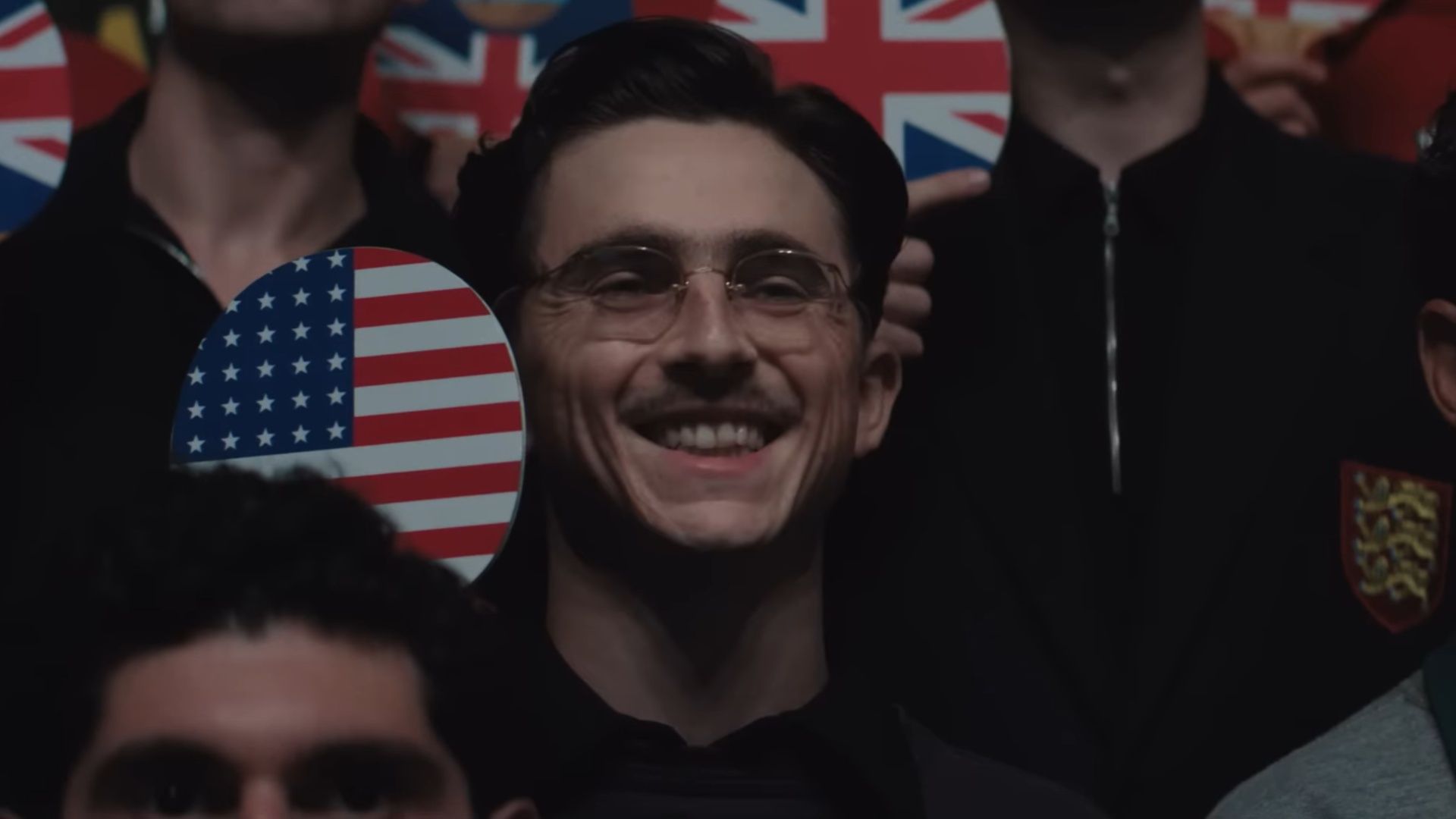 Person in a crowd smiling while holding a table tennis paddle painted with the United States flag.