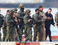 Nicolas Maduro and his wife, Cilia Flores, are seen in handcuffs after landing at a Manhattan helipad, escorted by heavily armed Federal agents as they make their way into an armored car en route to a Federal courthouse in Manhattan on January 5, 2026 in New York City. (Image via Getty)