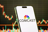 Logotipo da Comcast Corporation em smartphone com fundo gráfico do mercado de ações - Fonte: Getty