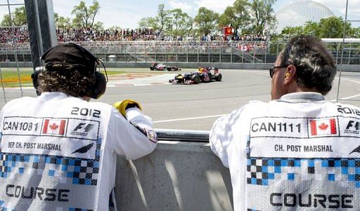 Course workers watch as Red Bull Racing Renault driver Sebastian Vettel makes his way around a turn