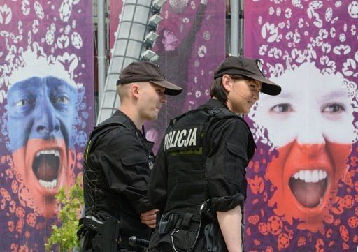 Police officers walk past a poster of a Russian (left) and Polish (right) fan at the National Stadium in Warsaw
