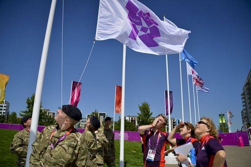 Volunteers watch soldiers raising a flag during the flag raising ceremony at the Olympic village