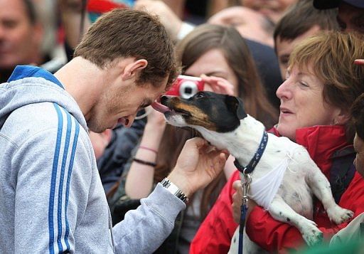 A dog licks British tennis player Andy Murray (L) as he meets with fans