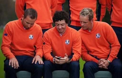 Rory McIlroy of Northern Ireland (C) shows Luke Donald of England (R) something on his iPhone