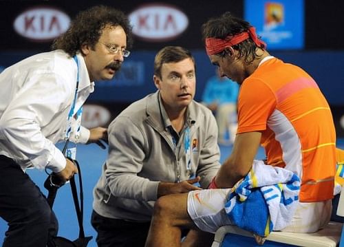 Courtside trainers attend to Rafael Nadal's knee injury during the Australian Open, in Melbourne, on January 26, 2010