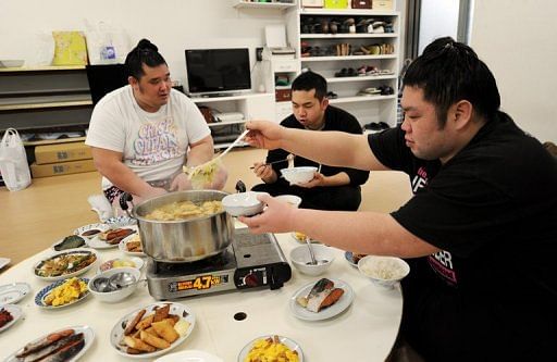 Sumo wrestlers Genkaiho (R) and Migikataagari (L) eat with hair dresser Tokonao at a sumo stable on February 14, 2013