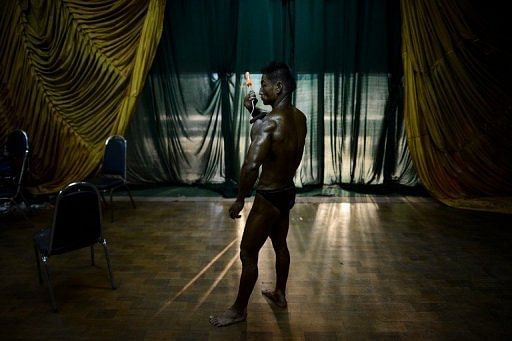 A bodybuilder applies tanning oil backstage ahead of the SEA Games selection contest in Yangon on February 12, 2013