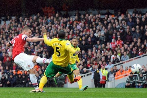 Arsenal&#039;s Lukas Podolski (L) scores a goal as Norwich City&#039;s Sebastien Bassong (C) ties to block, April 13, 2013