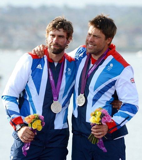 Britain&#039;s Andrew Simpson (R) and Iain Percy celebrate on the podium at the Olympics in Weymouth on August 5, 2012