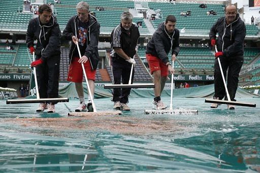 Employees remove water from a tarpaulin covering the Philippe Chatrier central tennis court in Paris on May 28, 2013