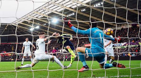 SWANSEA, WALES - JANUARY 14: Olivier Giroud (c) strokes in the first Arsenal goal past Lukasz Fabianski during the Premier League match between Swansea City and Arsenal at Liberty Stadium on January 14, 2017 in Swansea, Wales.  (Photo by Stu Forster/Getty Images)